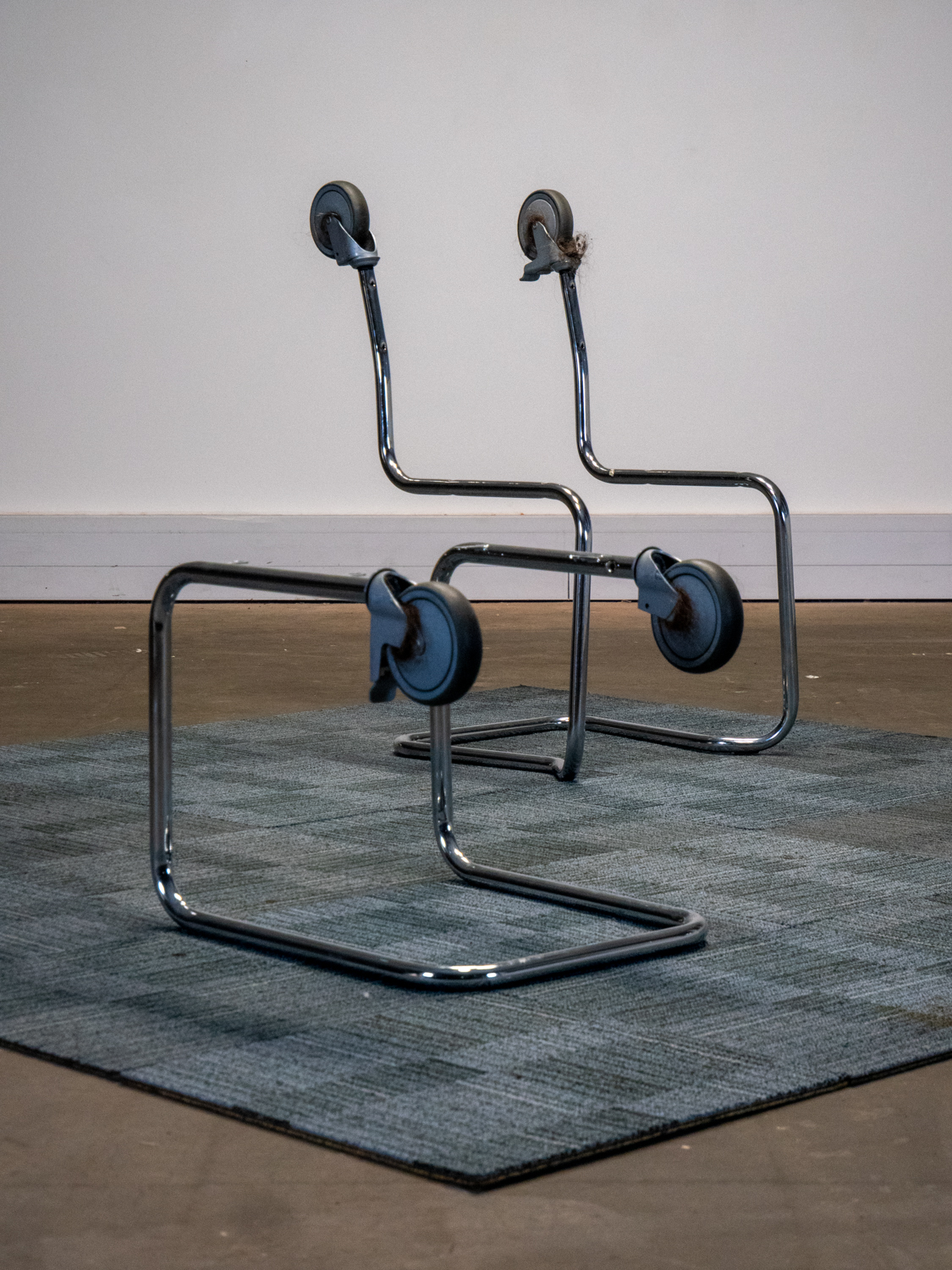 two chair frame sculpures with wheels on a square of carpet tiles